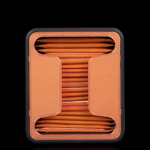 May include: A rectangular storage organiser with a black outer frame and a textured copper-coloured interior structure. The unit holds a stack of orange rectangular packets with thin red stripes, arranged horizontally within the central opening.