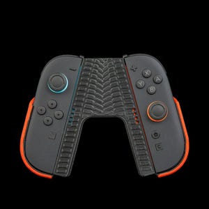 May include: Black and orange gaming controller with a textured center grip. The controller has a blue and orange joystick, and the buttons are labeled with letters and symbols. The controller is designed for a gaming console.