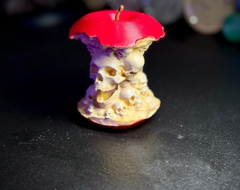 May include: A red apple with a bite taken out of it, revealing a cluster of white skulls inside. The apple is made of ceramic and is a decorative object.