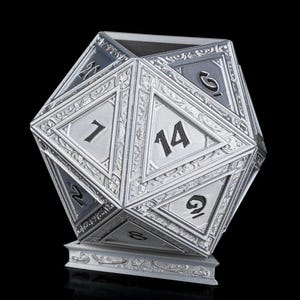 May include: A silver-colored, ornate, 14-sided die with numbers 1 through 14 on each face. The die is sitting on a base with intricate details.