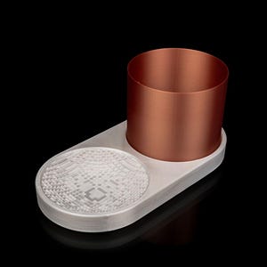 May include: A white oval-shaped coaster with a textured surface and a copper-coloured cup sitting on top.