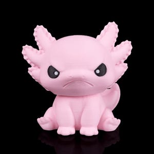 Puede incluir: Figura de axolotl rosa con expresión de enfado. La figura tiene ojos negros y branquias detalladas. El axolotl está sentado con las patas separadas y su cola es visible. El fondo es negro.