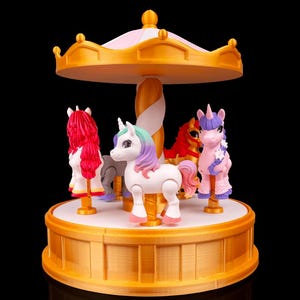 May include: A carousel toy featuring four unicorn figures in shades of pink, white, and red. The carousel has a gold-coloured roof and base, with a white and gold central support. The background is black.