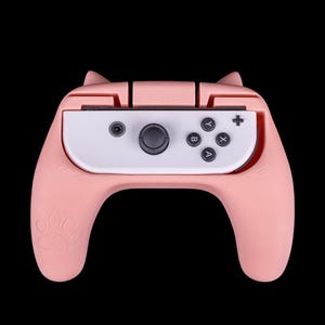 May include: A pink Nintendo Switch controller with paw print grips. The controller has a white faceplate with black buttons and a grey joystick.