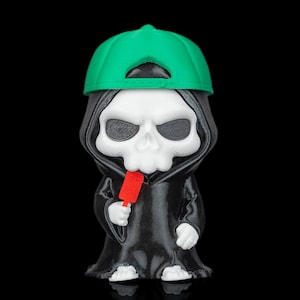 Peut inclure: Une petite figurine représentant un squelette portant une casquette de baseball vert vif et une robe à capuche noire. Le squelette a un crâne blanc et des mains blanches, et il tient un petit objet rectangulaire rouge dans sa main droite.