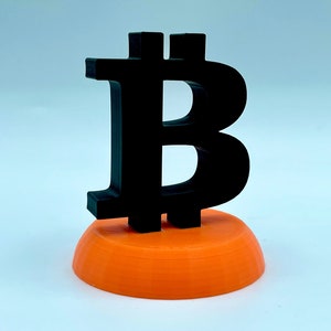 May include: A black 3D printed Bitcoin symbol on an orange base.
