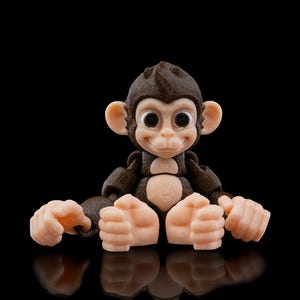May include: A small brown and beige monkey figurine with large eyes and a friendly expression. The monkey is sitting with its legs crossed and its hands resting on its knees.