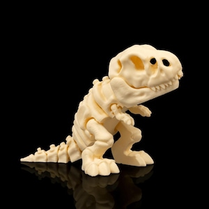 Pode incluir: Estatueta de esqueleto de Tyrannosaurus Rex creme. O modelo de dinossauro está em pé, com caixa torácica, crânio e ossos das pernas visíveis. A estatueta está em um fundo preto, com uma superfície reflexiva.