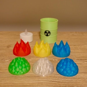 May include: A collection of colorful, flame-shaped and dome-shaped decorative objects. The flames are red, yellow, and blue. The domes are green, white, and blue. A green barrel with a biohazard symbol and a small white candle are also present.