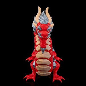 Può includere: Una statuetta di drago rosso e grigio con una lunga coda e quattro zampe. Il drago ha un'espressione feroce ed è in posizione eretta.