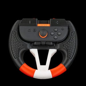 May include: Black and orange gaming steering wheel with white and red accents. The wheel has a central control panel with buttons and a joystick. The design includes a textured grip and is set against a black background.