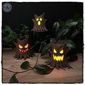 May include: Three brown tree stump sculptures with carved, glowing faces. One stump has a yellow oval-mouthed expression, while the other two feature jagged, toothy grins illuminated in orange and yellow light, creating a spooky, lit-up display.