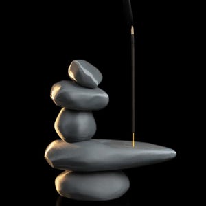 May include: A gray stone incense holder with a stack of smooth, rounded stones. An incense stick is lit, with smoke rising against a black background. The holder is designed to resemble a zen garden.