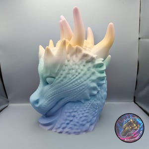 Può includere: Una scultura a testa di drago stampata in 3D in colori pastello. La testa del drago passa dal blu al verde, al giallo e al rosa. La scultura presenta squame e corna dettagliate. È visibile un logo circolare con una testa di drago.
