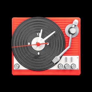 May include: A red and black turntable clock with white clock hands and a red second hand. The clock face resembles a vinyl record, with the numbers 12, 3, 6, and 9 visible. The clock has a silver tone arm and buttons.