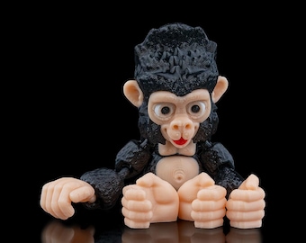 May include: A black and brown toy monkey figurine with a red mouth and large eyes. The monkey is sitting with its hands in front of it.