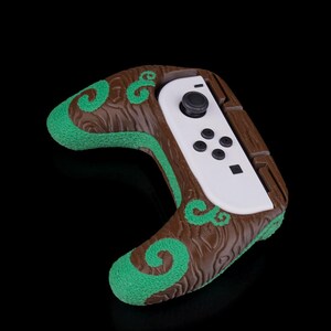 Könnte beinhalten: Ein weißer Nintendo Switch Joy-Con-Controller mit braunen und grünen, strukturierten Griffen. Die Griffe haben ein holzähnliches Muster mit grünen Wirbeln.