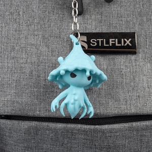 May include: A light blue keychain featuring a whimsical creature with a mushroom-like hat and multiple tentacles. The keychain is attached to a silver chain and a black key ring. A rectangular tag with the text "STLFLIX" is also attached.