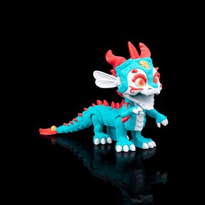 Puede incluir: Figura de dragón turquesa con detalles rojos, incluyendo cuernos y espinas. El dragón tiene detalles blancos en la cara y los pies, con un acento amarillo en la cola. El juguete está sobre un fondo negro.