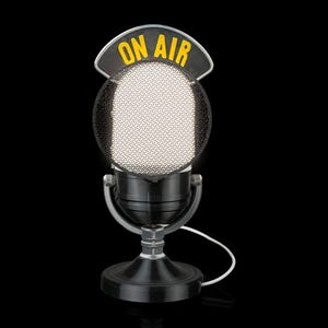 May include: A black vintage-style microphone with a mesh head and a base. The microphone has a yellow "ON AIR" sign above the head. A white cable extends from the base. The microphone is set against a black background.