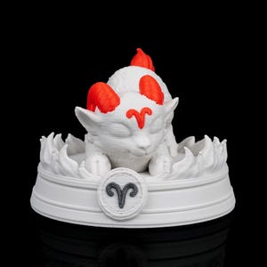 May include: A white figurine of a stylized ram, featuring red accents on its horns and forehead. The ram is seated on a white base with a gray Aries symbol. The sculpture is set against a black background.