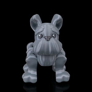 Könnte beinhalten: Graue 3D-gedruckte Bulldoggenfigur. Die Bulldogge hat große, ausdrucksstarke Augen, ein faltiges Gesicht und Schlappohren. Die Figur ist in einer sitzenden Position mit ausgestreckten Vorderpfoten dargestellt. Der Hintergrund ist schwarz.