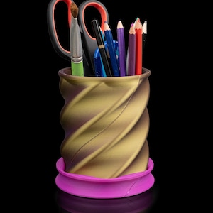 May include: A gold and brown swirl design desk organizer with a purple base. The organizer is filled with pencils, pens, and a pair of scissors.