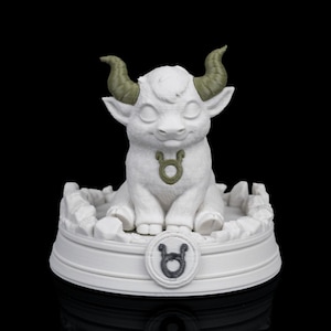 Op de afbeelding: Een witte Taurus dierenriem figuur met groene hoorns en een bijpassende groene Taurus symbool hanger. Het beeldje staat op een witte basis met het Taurus symbool en een getextureerde rand. De achtergrond is zwart.