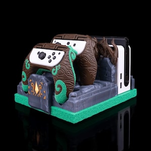 May include: A green and brown themed Nintendo Switch charging dock with two controllers. The dock is shaped like a stone structure with vines and a tree trunk. The controllers are also decorated with vines and a tree trunk pattern.