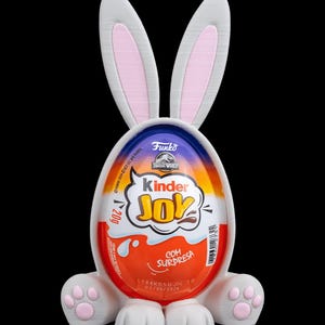 May include: A white 3D-printed Easter bunny-shaped holder cradling a Kinder Joy egg. The egg features a colorful design with the words "Kinder Joy" and "COM SURPRESA". The bunny has pink inner ears and paw pads.