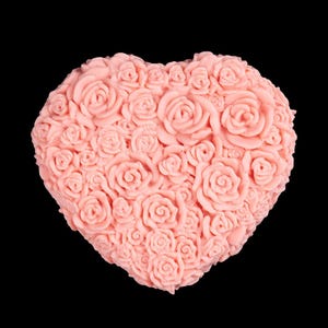 May include: A heart-shaped ornament, covered in small, detailed rose blossoms. The roses are a soft, muted pink colour, set against a solid black background. The item is likely made of soap or a similar material.