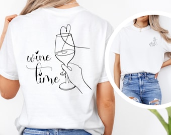 May include: White t-shirt with a black line drawing of a wine glass and the words "wine time". A smaller version of the design is on the front. The shirt is a casual, everyday wear item.