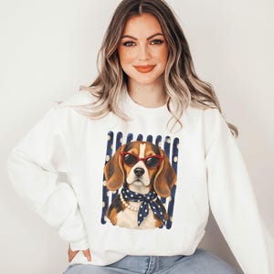 Könnte beinhalten: Ein weißes Langarm-Sweatshirt mit einem Grafikdruck eines Beagle-Hundes, der eine rote Katzenaugen-Sonnenbrille, eine Perlenkette und ein dunkelblaues, gepunktetes Halstuch trägt, vor einem Hintergrund aus vertikalen dunkelblauen und weißen Streifen.
