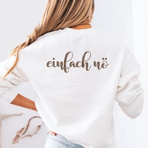 Könnte beinhalten: Ein weißes Langarm-Sweatshirt mit dem Schriftzug "einfach nö" auf der Rückseite in einem braun-schwarzen Leopardenmuster. Das Kleidungsstück hat einen Rundhalsausschnitt und lange Ärmel, wobei der Text in einer kursiven Schriftart gehalten ist.
