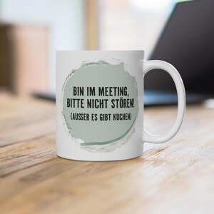 Könnte beinhalten: Eine weiße Keramiktasse mit einem kreisförmigen, salbeigrünen Aquarell-Motiv und dem schwarzen Text: BIN IM MEETING, BITTE NICHT STÖREN! (AUSSER ES GIBT KUCHEN). Die Tasse verfügt über einen Standardhenkel und eine glatte, glänzende Oberfläche.