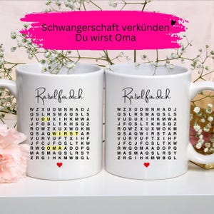 May include: Two white ceramic mugs featuring a black printed word search puzzle titled Ratsel fur dich. The puzzle contains highlighted letters spelling Du wirst Oma. Each mug has a small red heart icon at the bottom and a handle on the side.