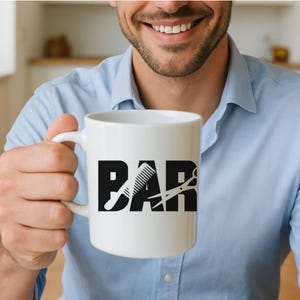 May include: White ceramic mug with the word "BAR" in bold black letters, with a comb and scissors graphic. The mug is held by a person wearing a light blue button-down shirt.