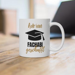Peut inclure: Un mug en céramique blanche avec le prénom Adrian écrit en lettres dorées, une icône de toque de diplômé noire et le texte FACHABI geschafft en noir et or. Le mug possède une anse standard et un corps cylindrique lisse et brillant.