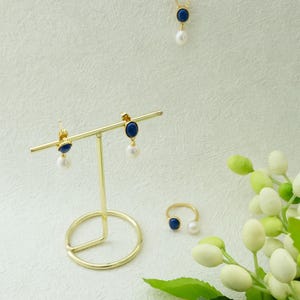 K&ouml;nnte beinhalten: Ein Satz Goldschmuck mit blauen und wei&szlig;en Steinen. Das Set beinhaltet eine Halskette, Ohrringe und einen Ring. Der Schmuck wird auf einem goldenen St&auml;nder vor einem wei&szlig;en Hintergrund pr&auml;sentiert.