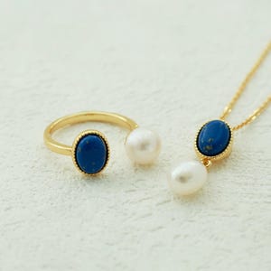 K&ouml;nnte beinhalten: Ein goldener Ring- und Halskettensatz mit blauen ovalen Steinen und wei&szlig;en Perlenakzenten.