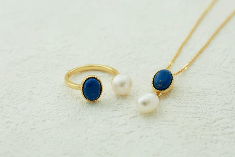K&ouml;nnte beinhalten: Ein goldener Ring- und Halskettensatz mit blauen ovalen Steinen und wei&szlig;en Perlenakzenten.