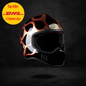 May include: Black motorcycle helmet with a flame design in gold and red. The helmet has a glossy finish and a black visor. The word "CHAMBER" is visible on the helmet.