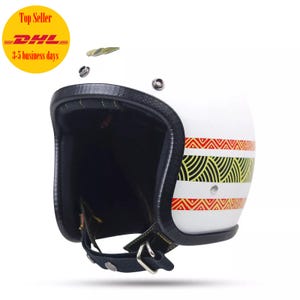 May include: White motorcycle helmet with a black leather strap and a geometric pattern in red, yellow, and black.