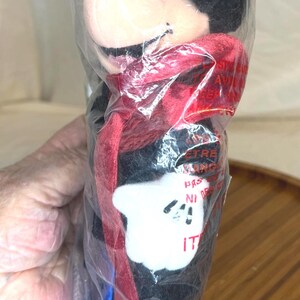 K&ouml;nnte beinhalten: Ein Mickey Mouse Pl&uuml;schtier in einer durchsichtigen Plastikt&uuml;te. Das Pl&uuml;schtier hat einen schwarzen K&ouml;rper, einen roten Schal und wei&szlig;e Handschuhe. Die Verpackung hat Text.