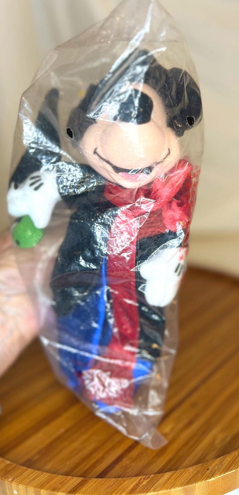 K&ouml;nnte beinhalten: Ein Mickey Mouse Pl&uuml;schtier in einer durchsichtigen Plastikt&uuml;te. Das Pl&uuml;schtier hat einen schwarzen Kopf und Ohren, einen roten Schal und eine blaue Hose. Es h&auml;lt einen gr&uuml;nen Gegenstand in seiner wei&szlig;en behandschuhten Hand.