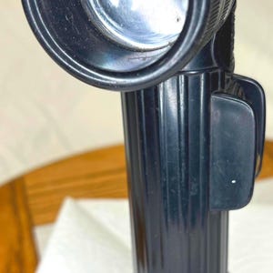 Peut inclure: Une lampe torche noire à angle droit avec un manche cylindrique strié et une tête circulaire dotée d'un intérieur réfléchissant. L'appareil comprend un clip latéral et une prise texturée, conçue pour une utilisation manuelle avec une lentille claire.