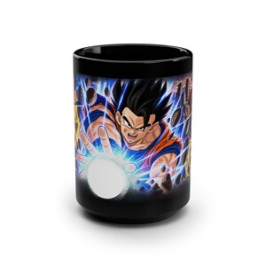 Può includere: Una tazza in ceramica nera con una vivace illustrazione grafica di un personaggio dai capelli scuri in un completo arancione e blu, che tende la mano per emettere una sfera di energia bianca luminosa circondata da fulmini blu e rocce.
