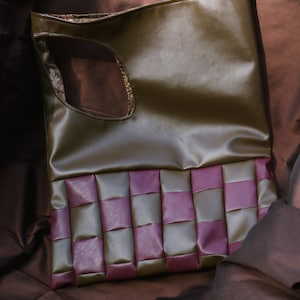 May include: A green faux leather tote bag with a woven purple and green bottom. The bag has a cut-out handle.