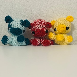 May include: Three crocheted stuffed animals. The first is a blue and white cow, the second is a red and white pig, and the third is a yellow duck.