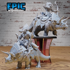 May include: Two gray miniature figurines of fantasy characters riding triceratops. One figure holds a spear, the other a bow and arrow. The figurines are on a wooden surface with a brick wall background. The text "EPIC Miniatures" is in the upper left corner.